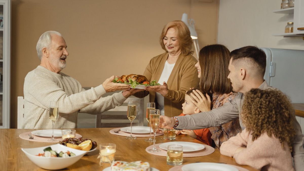 A family passes a holiday platter across a dinner table set with plates, glasses and side dishes