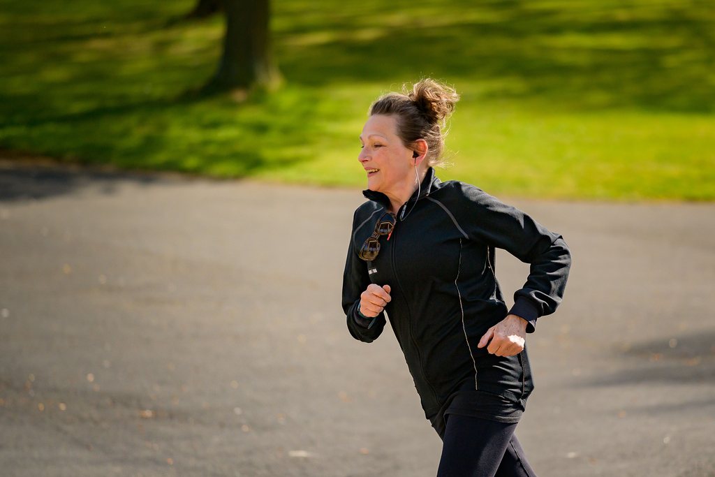 A smiling woman jogging on a sunny park path